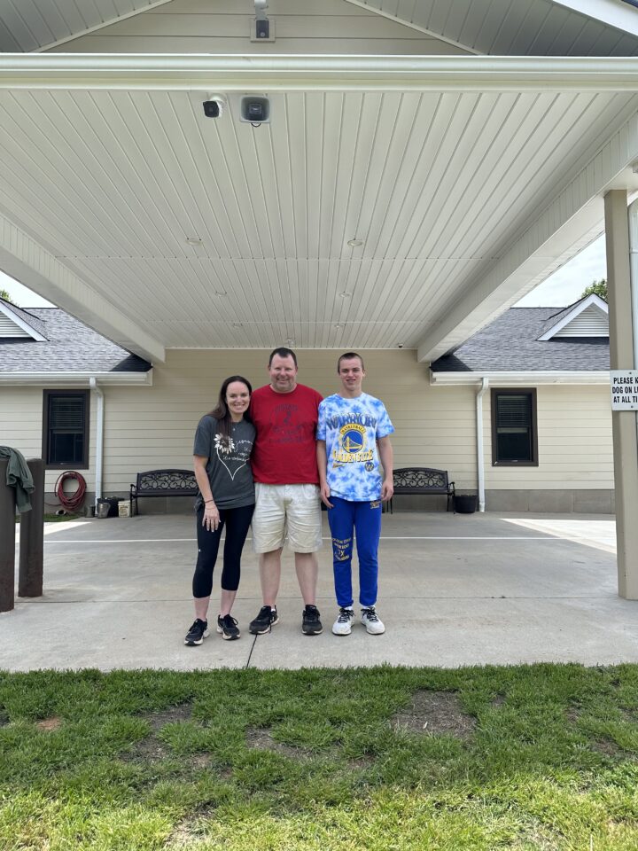 Mom and dad and teenage son standing in front of a dog kennel